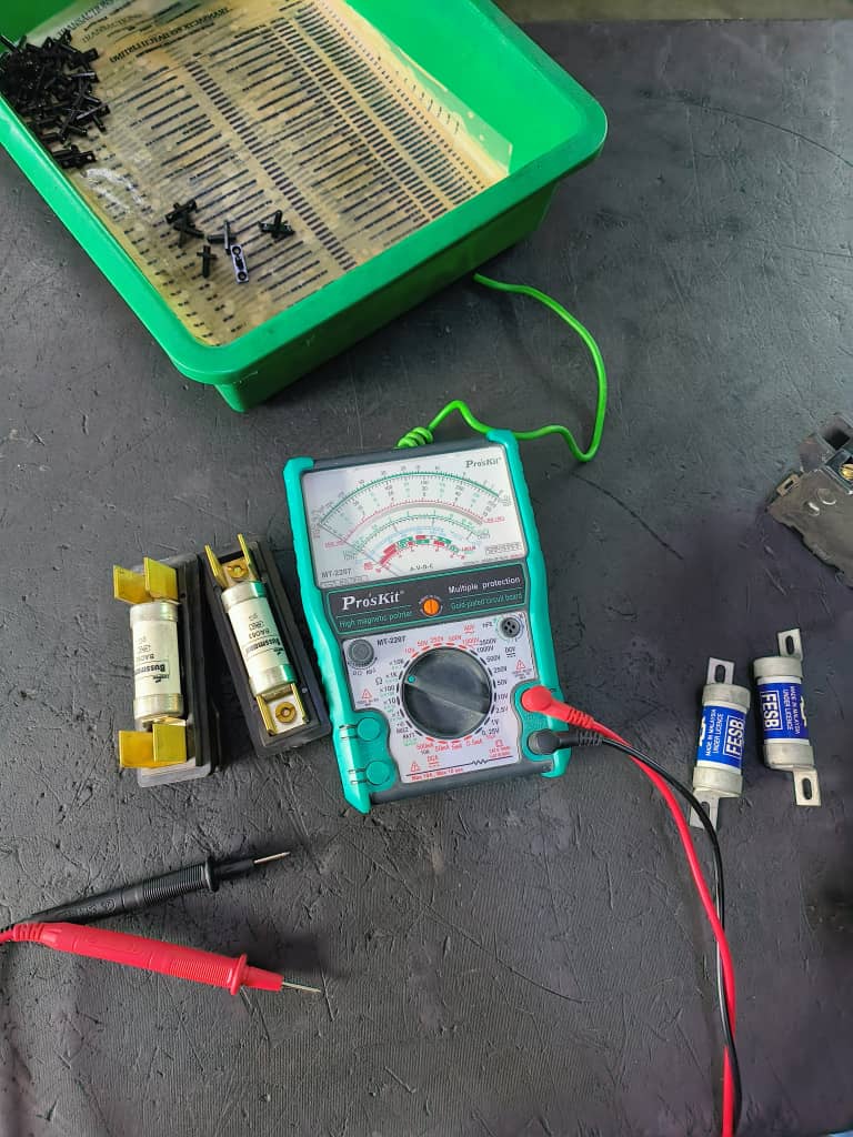 Analog multimeter with HRC industrial fuses and test probes on a workshop bench