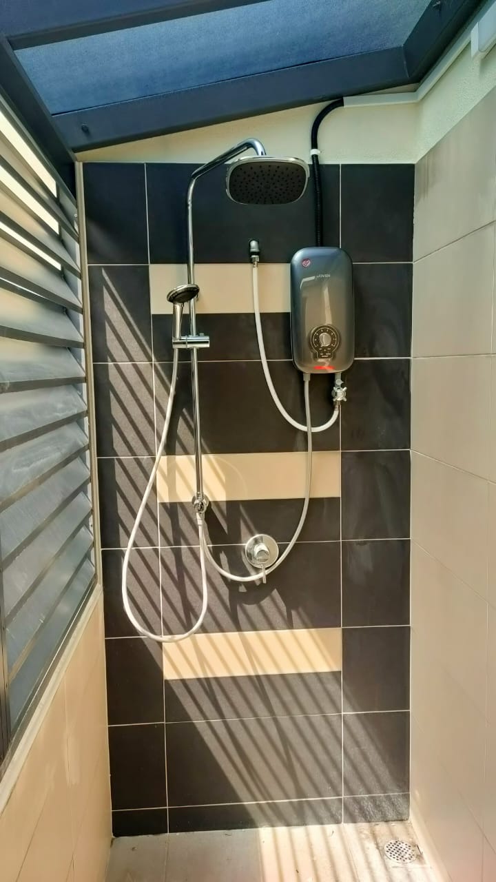 JOVEN instant electric water heater installed in a tiled commercial shower stall with rain showerhead and chrome plumbing